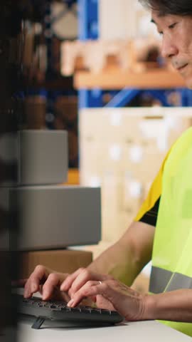 Vertical Video Man in hi vis vest reviews shipment details on awb tags for dispatch in industrial warehouse, parcels from the storage racks with tracking numbers for seamless express delivery. Camera