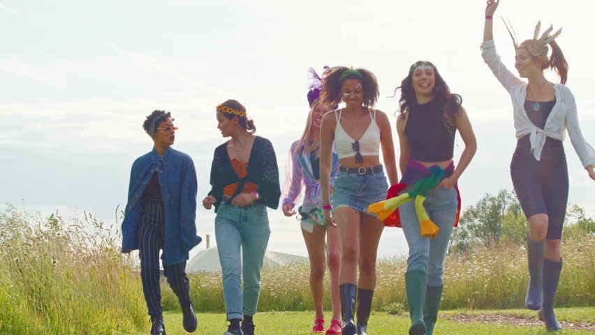 Group of young female friends dressed up and wearing headdresses walking through music festival site- shot in slow motion