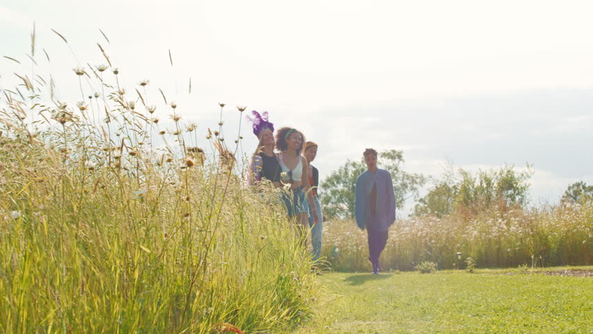 Group of young female friends dressed up and wearing headdresses walking through music festival site- shot in slow motion