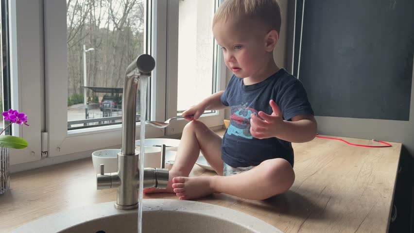 A playful toddler joyfully exploring the flowing water at the kitchen sink, showcasing curiosity and childhood delight