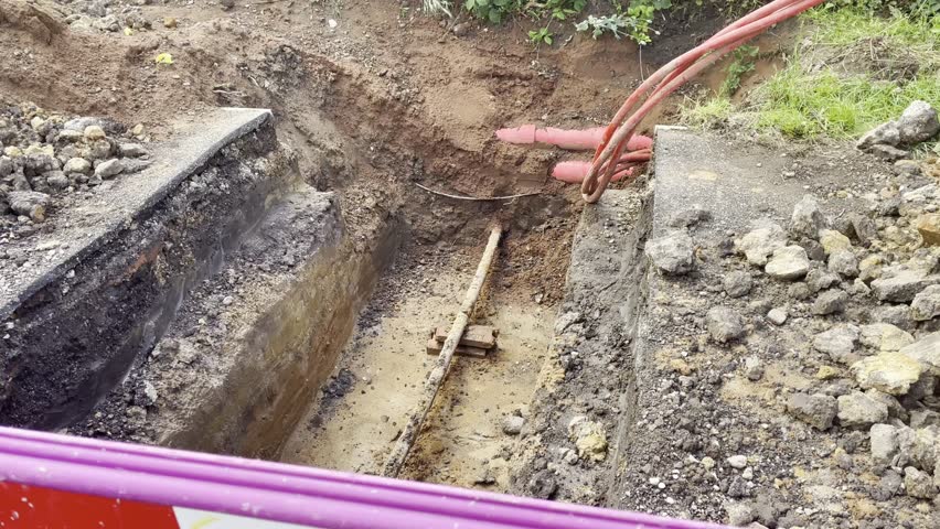 A construction site with exposed ground showing soil layers, red underground cables, and surrounding earthworks. Ideal for depicting infrastructure work, excavation projects