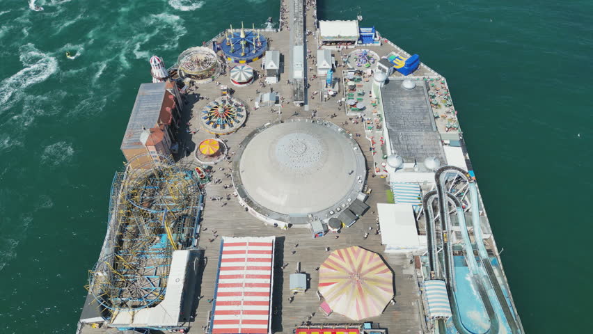 Drone view of a pier with amusement park over turquoise water. 