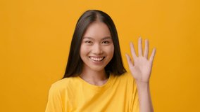 Millennial Asian woman smiling and waving against a bright yellow backdrop - Powered by Shutterstock - Get 15% off with code: PIKWIZARD15