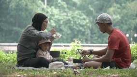 Happy Muslim family enjoying outdoor picnic, eating together on grass with child, relaxing in nature, bonding moment. sstkTravel - Powered by Shutterstock - Get 15% off with code: PIKWIZARD15