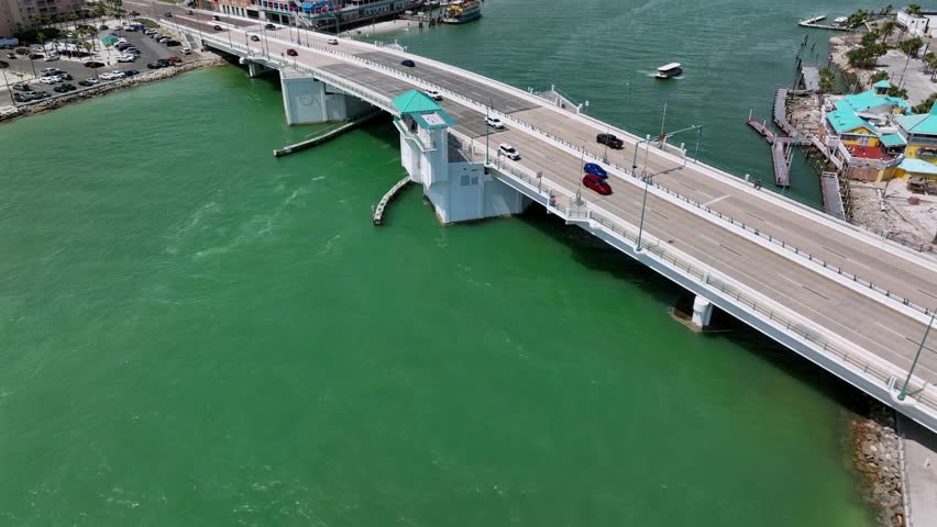 Cars on bridge crossing Johns Pass Channel with sunny day. Madeira Beach, Florida. Aerial orbit wide shot. Islands of Florida in background.