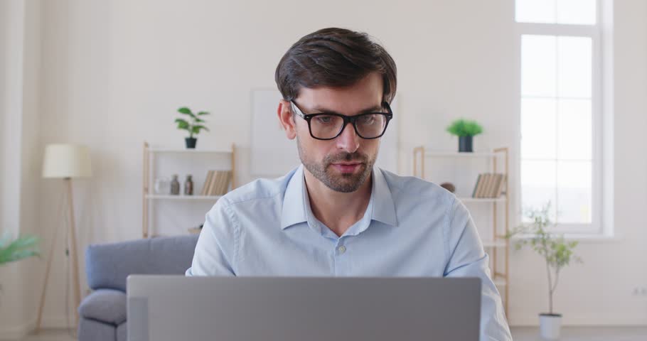 Tired young overworked business man suffering from headache after long hours computer work and taking off glasses sitting at desk on workplace in office in front of laptop. 4k video.