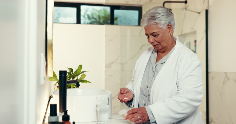 Senior woman, bathroom or medication with water for morning prescription or chronic illness in home. Elderly, female person or drinking mineral liquid with pills for medical symptoms or cure in house