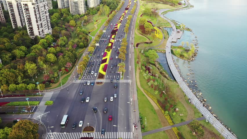 An aerial view captures the movement of vehicles on the main road through Suzhou Park. Lush greenery and water features line the road, creating an attractive urban environment.