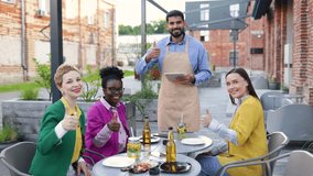 Happy group of friends and a waiter giving thumbs up in a restaurant outdoor setting. - Powered by Shutterstock - Get 15% off with code: PIKWIZARD15