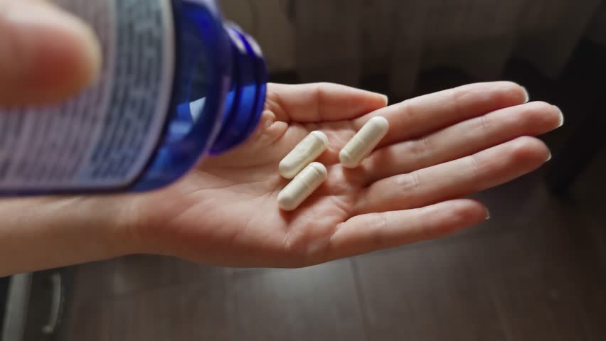 person pouring white supplement tablets from a blue bottle into their hand. Daily health care, vitamin intake, medication or nutritional supplement routine. Sport nutrition supplement 