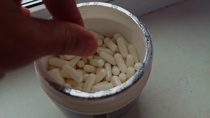 man hand take sport supplement pills. container filled with white capsules, suggesting daily supplements, medication, or vitamins for health and wellness. daily dose dietary supplement oral medication