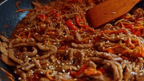 stir-fried pork with julienned carrots and bell peppers in a savory sauce, topped with sesame seeds. Hot dish being cooked in wok with wooden spatula, Asian-style home cooking. Thai food exotic flavor - Powered by Shutterstock - Get 15% off with code: PIKWIZARD15