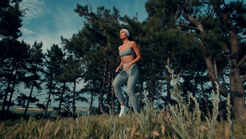 A beautiful, fit athlete runs powerfully in a forest meadow. Her focused mind and determined pace shine through in every step of this active moment.