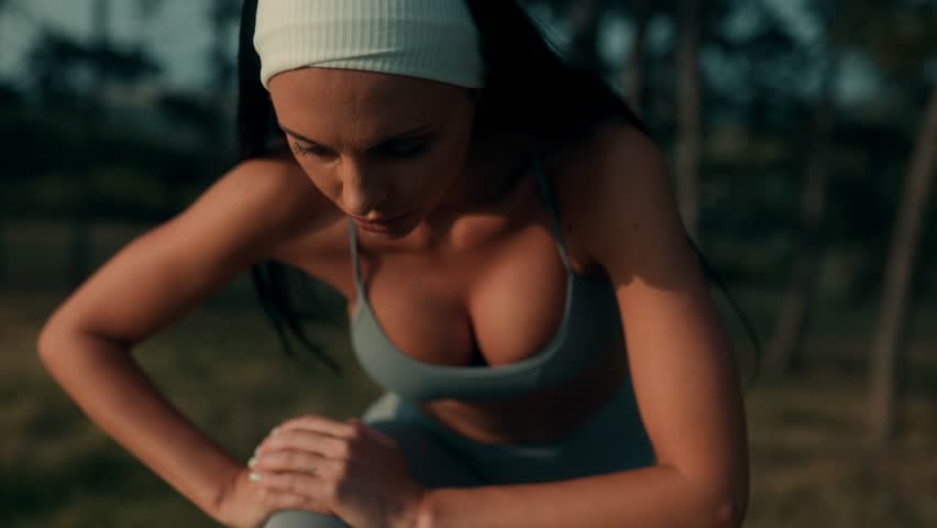 A strong young woman takes a breather after training outdoors. Leaning forward with focus, she shows determination, effort, and a fit, disciplined lifestyle.