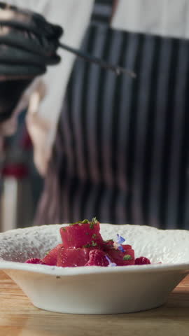 Vertical shot of chef garnishing tuna appetizer with edible flowers while serving food in restaurant