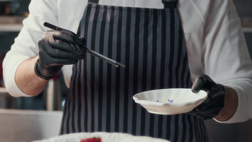 Zoom out shot of male chef garnishing tuna fillet cubes with edible flowers on plate before serving in fine dining restaurant