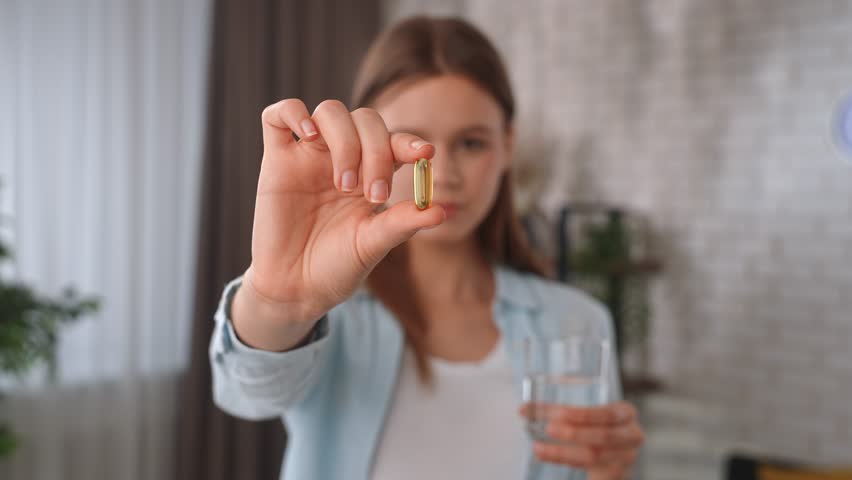 A person holds a nutritional supplement capsule and bottle, focusing on health through vitamins or supplements. Healthy living concept, taking vitamins for skin and hair beauty.