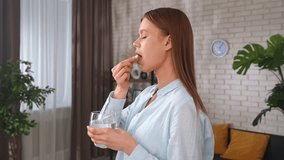 A young woman takes a pill and drinks water from a glass, symbolizing health, well-being and daily routine. Concept of healthy lifestyle, taking vitamins for beauty of skin and hair. - Powered by Shutterstock - Get 15% off with code: PIKWIZARD15