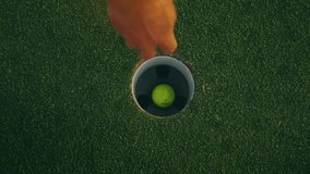 Top-down slow motion shot of a yellow golf ball rolling into the cup, bouncing inside the hole, while a male golfer’s arm reaches in to retrieve it. A close, dynamic moment capturing golf precision. - Powered by Shutterstock - Get 15% off with code: PIKWIZARD15