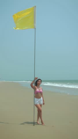 A woman standing next to a yellow flag on the beach, enjoying the peaceful day