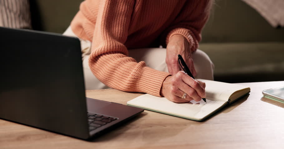 Hand, laptop and writing with person in living room of home for planning or reminder of tasks. Computer, notebook and to do list with senior woman in apartment for agenda, checklist or event schedule