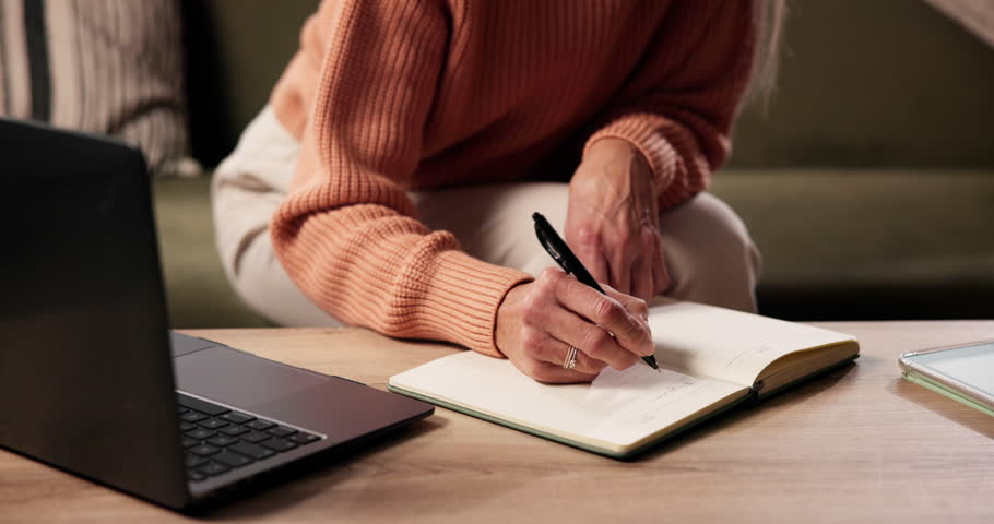 Hand, laptop and writing with person in living room of home for planning or reminder of tasks. Computer, notebook and to do list with senior woman in apartment for agenda, checklist or event schedule