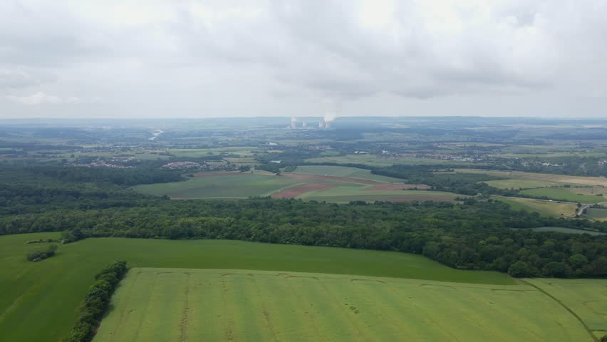 Nuclear power plant cooling towers in distance of open grass field, aerial drone France