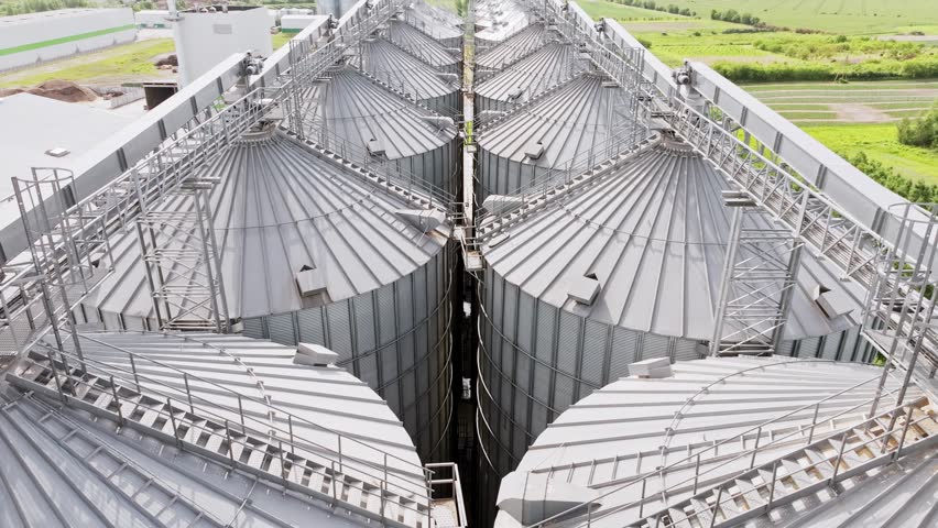 Smooth low drone flight moves forward above shiny silver grain silos in Latvia