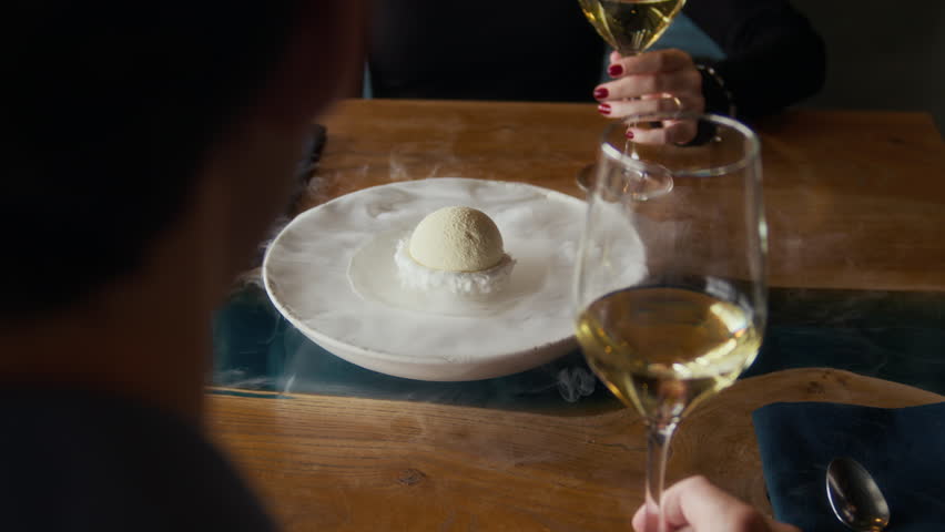 Medium close up shot of hands of unrecognizable waiter adding liquid nitrogen to sophisticated dessert of guests sitting at table having date with wine in restaurant