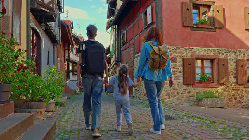 Woman with backpack and children walking on the beautiful street full of colorful houses with flowers of Eguisheim, France 