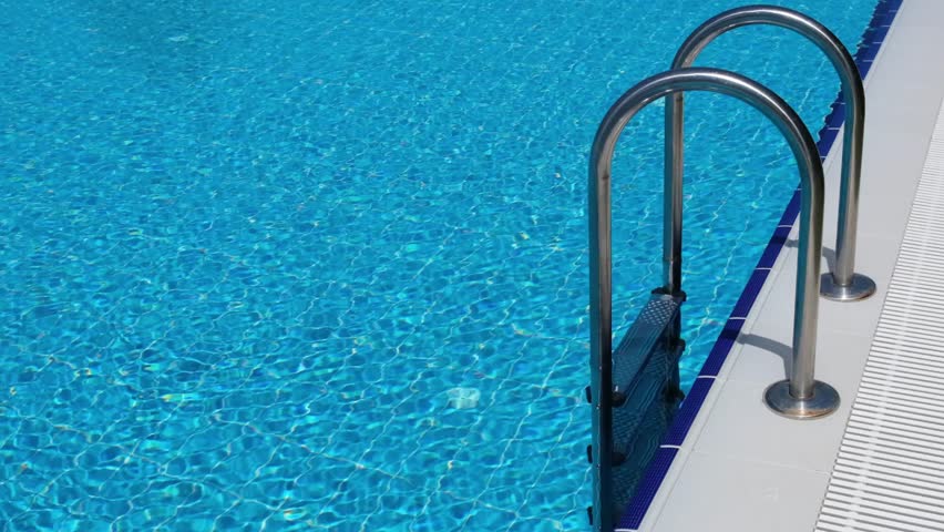 Enjoy a bright summer day by the swimming pool with shimmering blue water and metal ladders, inviting relaxation and leisure activities throughout the day.