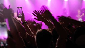 Enthusiastic concert crowd silhouetted under vibrant purple lighting, waving hands and capturing live music performance moments using smartphones - Powered by Shutterstock - Get 15% off with code: PIKWIZARD15