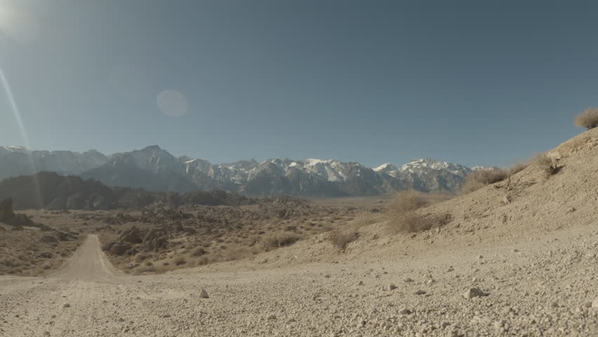 A vehicle drives over the camera along a dirt road towards Mt. Whitney and the Eastern Sierra Nevada snow-capped mountains