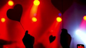 Silhouetted hands holding heart shaped paper cutouts sway rhythmically in a dimly lit concert venue, illuminated by vibrant red and blue spotlights - Powered by Shutterstock - Get 15% off with code: PIKWIZARD15