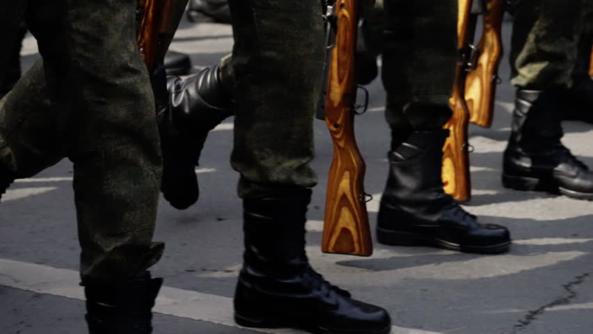 Close-up view of soldiers marching in formation with wooden-stock rifles, showcasing disciplined military movement, uniformed boots, and synchronized steps outdoors