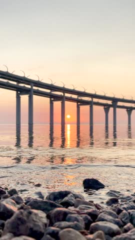 Beautiful sunset over the sea. The sun setting between the pillars of the bridge. Reflection of sunlight on water. Kanonersky Island, Saint-Petersburg. Vertical FullHD slow motion footage.