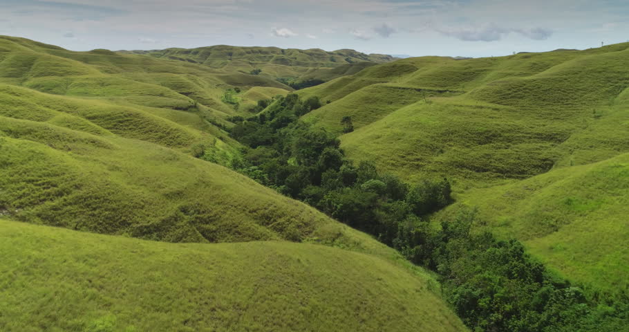 Rolling green hills stretch as far as the eye can see across Sumba island, Indonesia, captured in a breathtaking aerial view showcasing the untouched beauty of nature