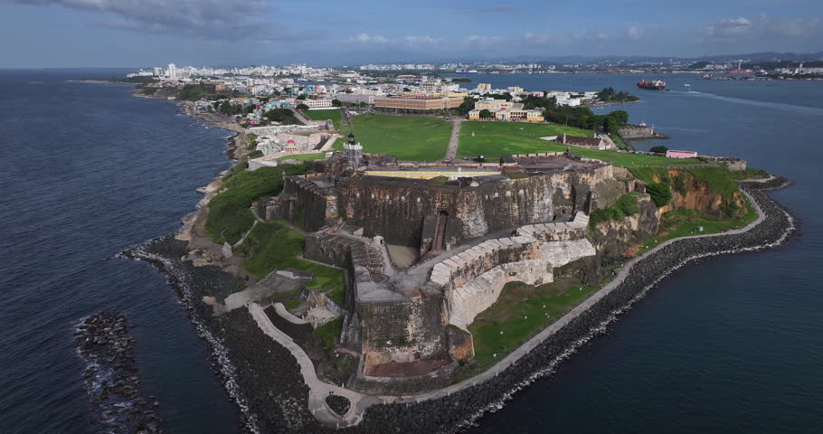 A sweeping drone shot capturing the historic Castillo San Felipe del Morro with the colorful buildings of Old San Juan in the background.