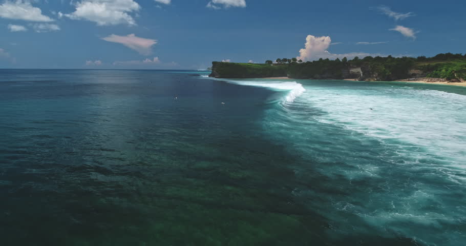 Stunning aerial view of Dreamland Beach in Bali, Indonesia, featuring vibrant turquoise waters, gentle waves on white sand, and lush green cliffs under a bright blue sky