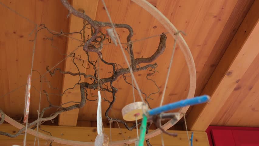 Handmade mobile crafted from twisted branches, wood slices, and repurposed objects, hanging under a wooden roof in a forest kindergarten setting.