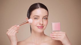 Woman makes makeup. Young woman makes blush on the face using makeup brush. Cosmetic concept. Beautiful brunette model doing make-up. Girl runs a makeup brush over her face - Powered by Shutterstock - Get 15% off with code: PIKWIZARD15