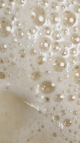 Beer pouring and splashing in super slow motion with visible foam and bubbles. Close-up macro shot capturing refreshing texture and movement, perfect for beverage commercials or drink promos.