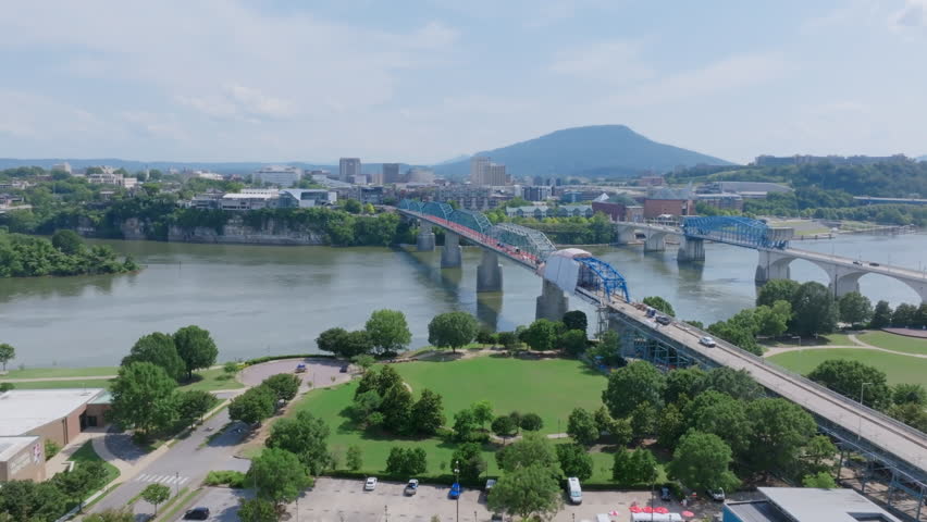 An aerial view of downtown Chattanooga, TN, showcases the Walnut Street Bridge under renovation, with the Tennessee River and Lookout Mountain visible in the background.