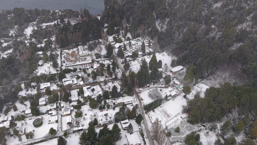 Drone gliding under heavy snowfall in Colonia Suiza, a town in San Carlos de Bariloche at the foot of Cerro López, covered in snow from above during a heavy winter storm in the Argentine Andes.