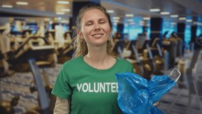 Young woman raises hand to show peace within gym as volunteer wearing glove holds bag while smile frames face near treadmill promoting fitness. - Powered by Shutterstock - Get 15% off with code: PIKWIZARD15