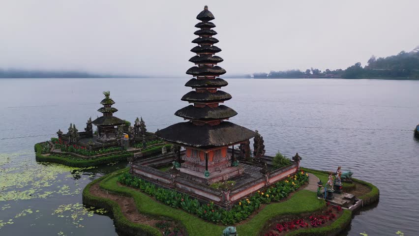 This cinematic drone footage features the peaceful Ulun Danu Beratan Temple on Lake Beratan, with reflections of the temple’s structure shimmering on tranquil waters beneath mountain peaks.