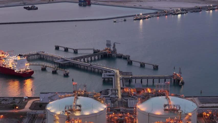 LNG tanker docked at an offshore terminal with multiple pipelines, storage tanks, and an industrial complex. Captures global energy logistics	
