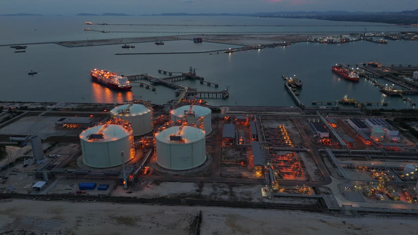 LNG tanker docked at an offshore terminal with multiple pipelines, storage tanks, and an industrial complex. Captures global energy logistics	
