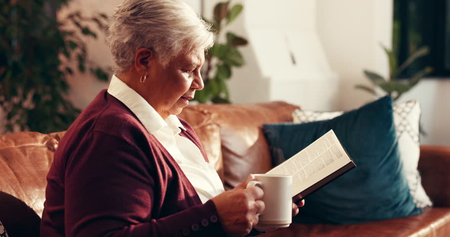 Coffee, reading book and relax with senior woman on sofa in living room of home for belief or faith. Bible, retirement and storytelling with Christian person drinking beverage in apartment for break