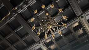 A grand, ornate golden chandelier with multiple candle-like lights hangs from a dark, coffered ceiling, showcasing intricate historical design and creating a rich ambiance - Powered by Shutterstock - Get 15% off with code: PIKWIZARD15